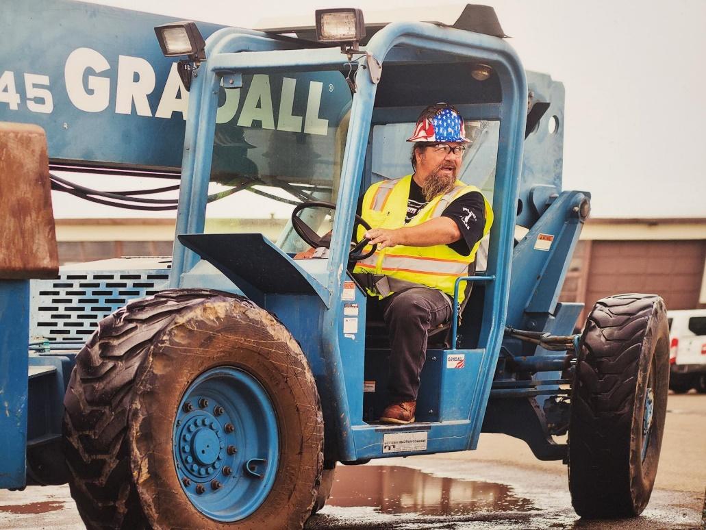 Operator in construction vehicle wearing safety gear.