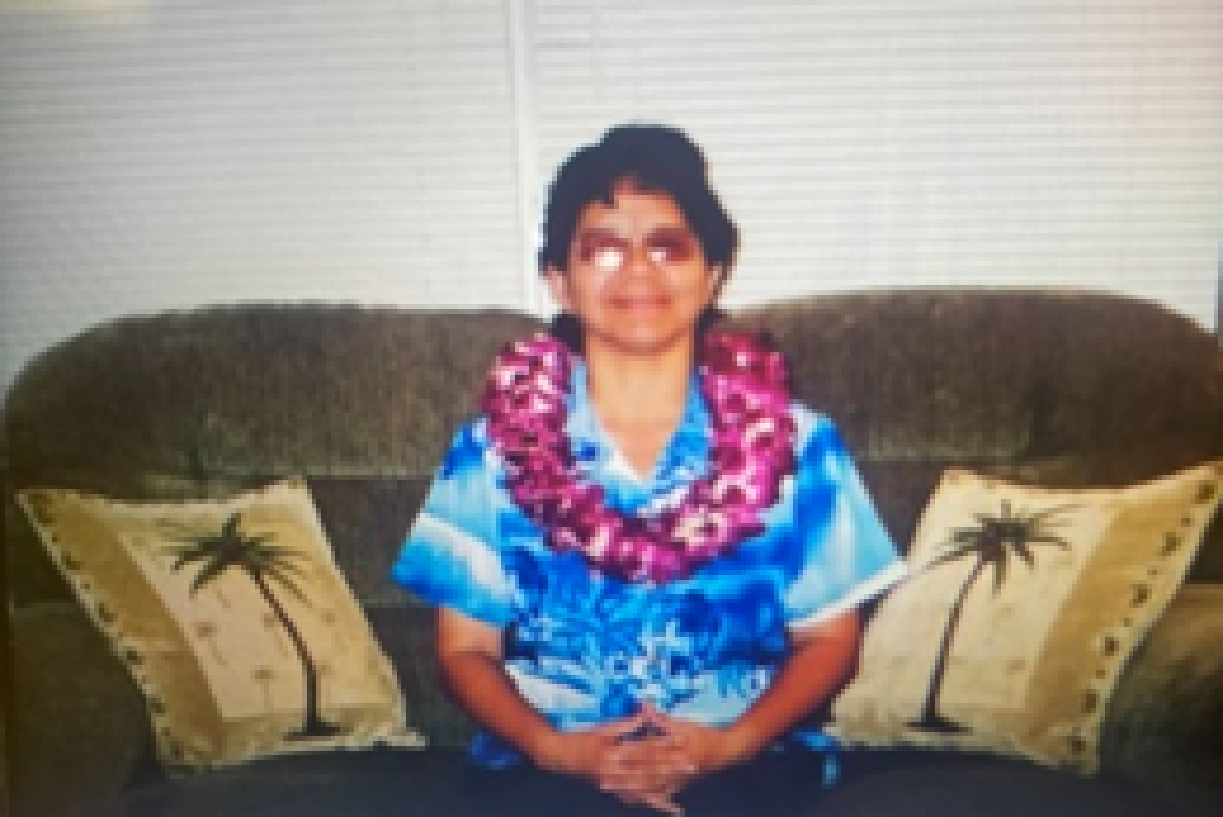 Person with lei on sofa, palm pillows.