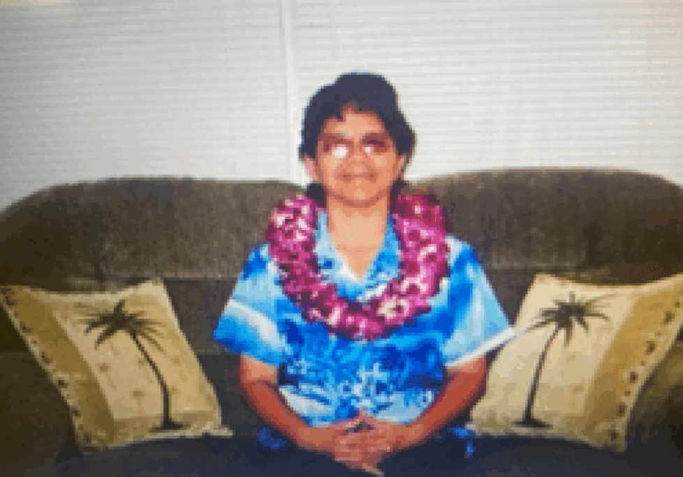 Person with lei on sofa, palm pillows.