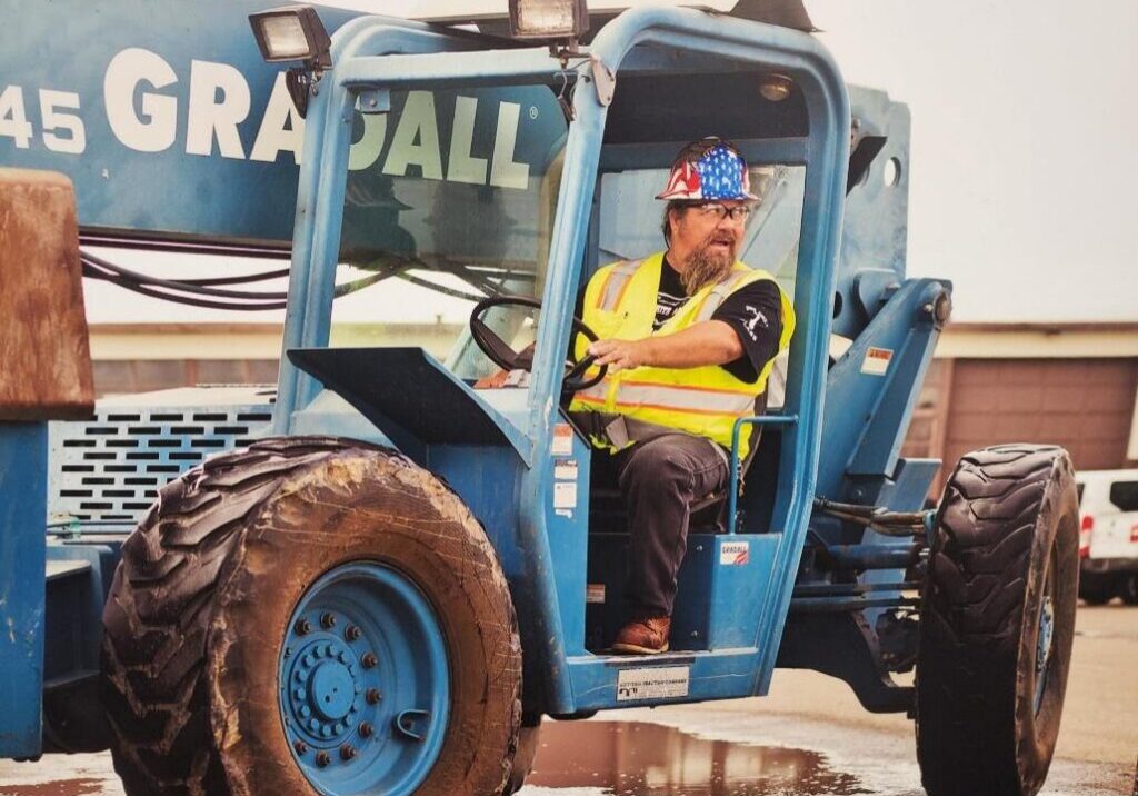 Operator in construction vehicle wearing safety gear.